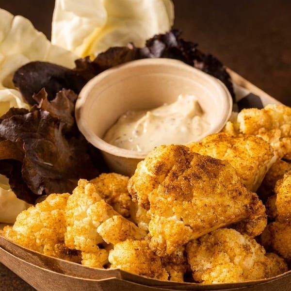 Crispy fried cauliflower bites with a side of creamy dip and fresh lettuce in a paper tray.