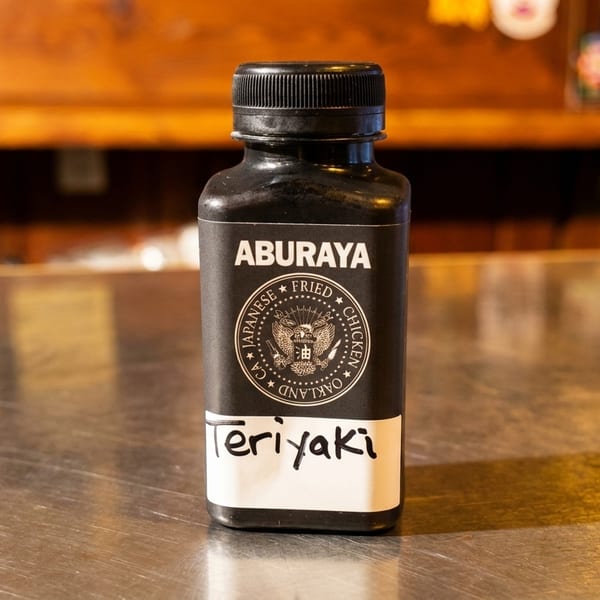 Aburaya Japanese Fried Chicken Teriyaki sauce bottle on a metallic counter with a wooden background.