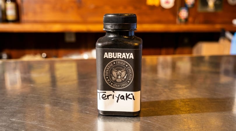 Aburaya Japanese Fried Chicken Teriyaki sauce bottle on a metallic counter with a wooden background.