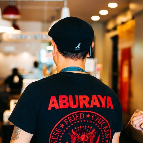 Back of a person wearing a black "Aburaya Japanese Fried Chicken" t-shirt in a restaurant.