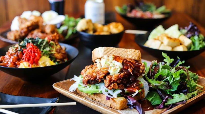 A fried chicken sandwich with coleslaw and BBQ sauce, served with a side salad.