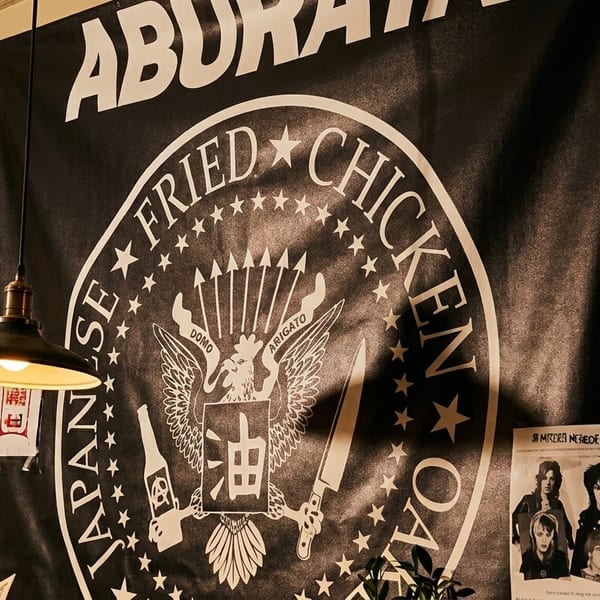 A black banner with "Japanese Fried Chicken" and a chicken logo hangs on a wall with posters.
