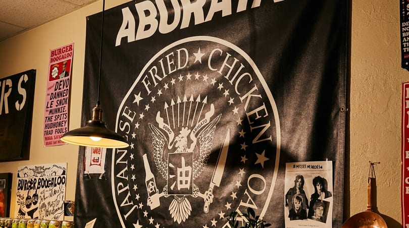 A black banner with "Japanese Fried Chicken" and a chicken logo hangs on a wall with posters.
