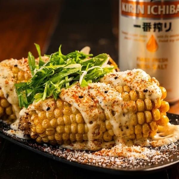 Grilled corn on the cob with creamy sauce, spices, and greens, next to a Kirin Ichiban can.