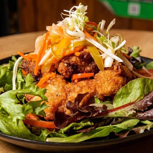 Crispy fried chicken pieces on a bed of mixed greens, topped with pickled vegetables and tomatoes.