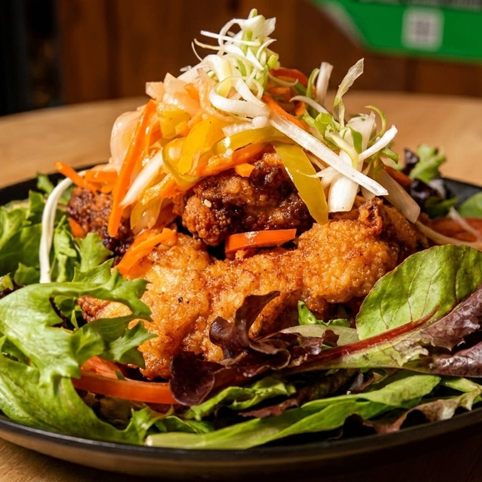 Crispy fried chicken pieces on a bed of mixed greens, topped with pickled vegetables and tomatoes.