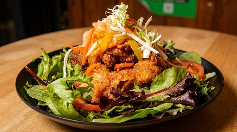 Crispy fried chicken pieces on a bed of mixed greens, topped with pickled vegetables and tomatoes.
