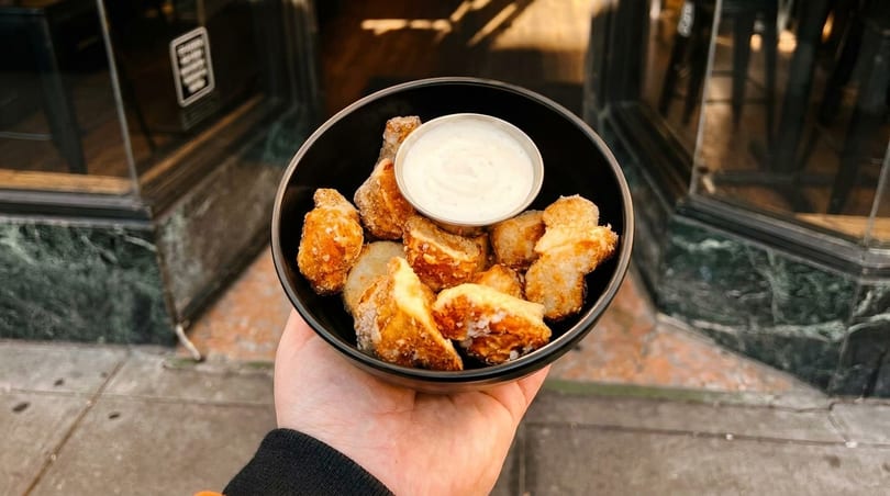 Hand holding a black bowl of fried cheese curds with a side of ranch dressing.