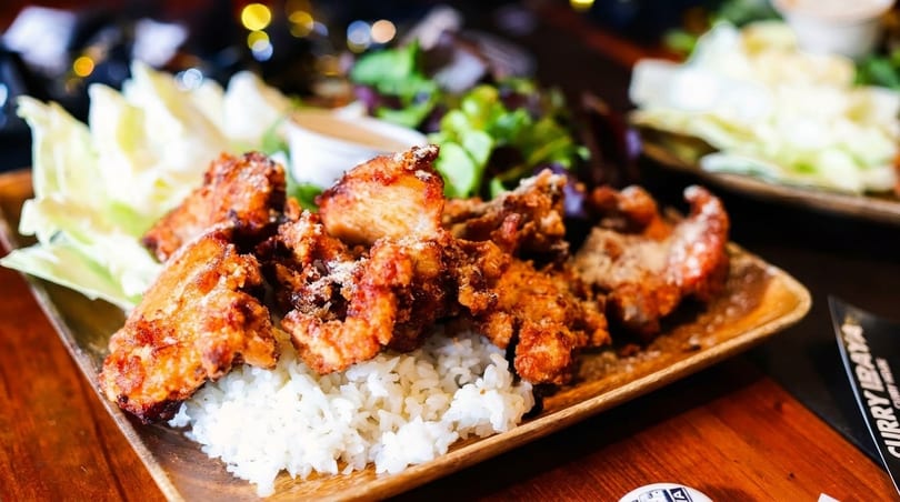 Crispy fried chicken karaage with white rice, cabbage, and a side salad on a wooden plate.