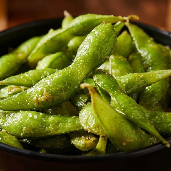 Close-up of a black bowl filled with vibrant green edamame pods, lightly salted.