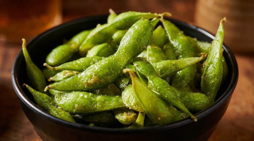 Close-up of a black bowl filled with vibrant green edamame pods, lightly salted.